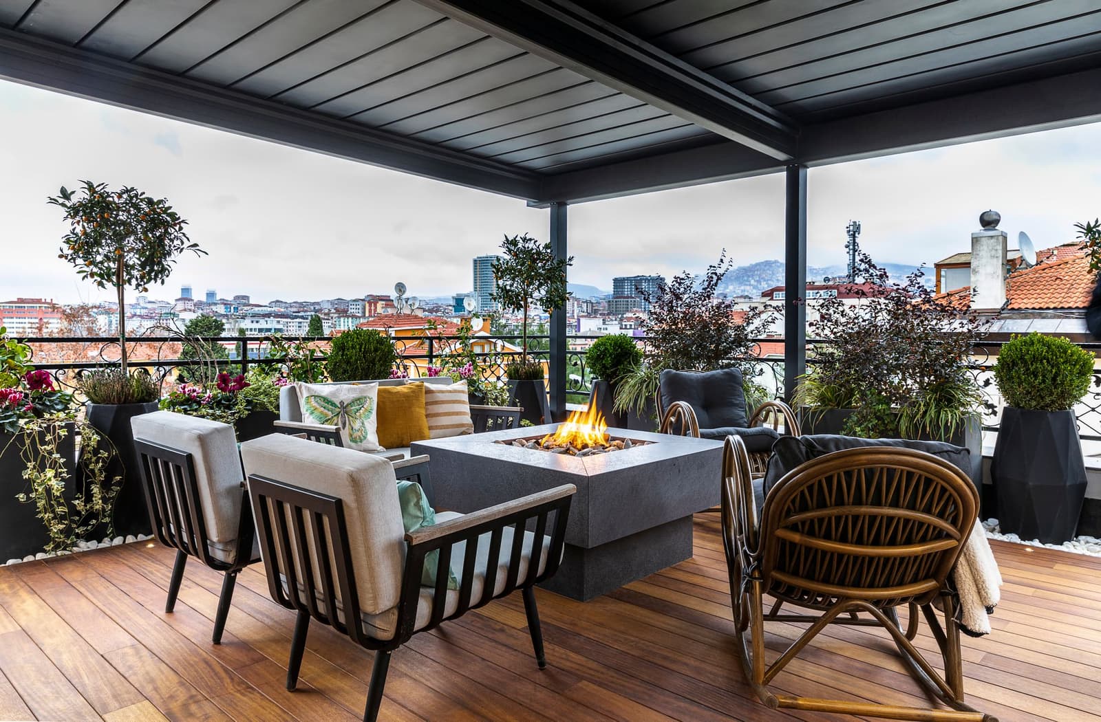 Terraza cubierta con sillones, plantas y un fuego de gas